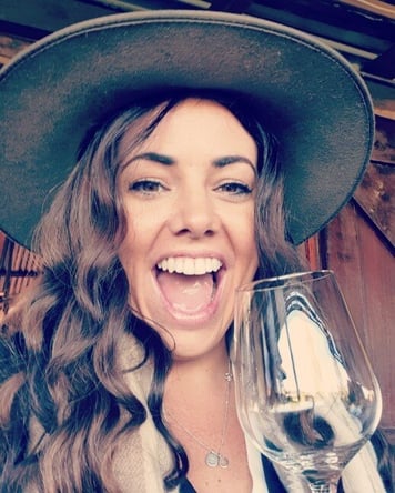 A person in a cowboy hat holding a glass of wine

Description automatically generated